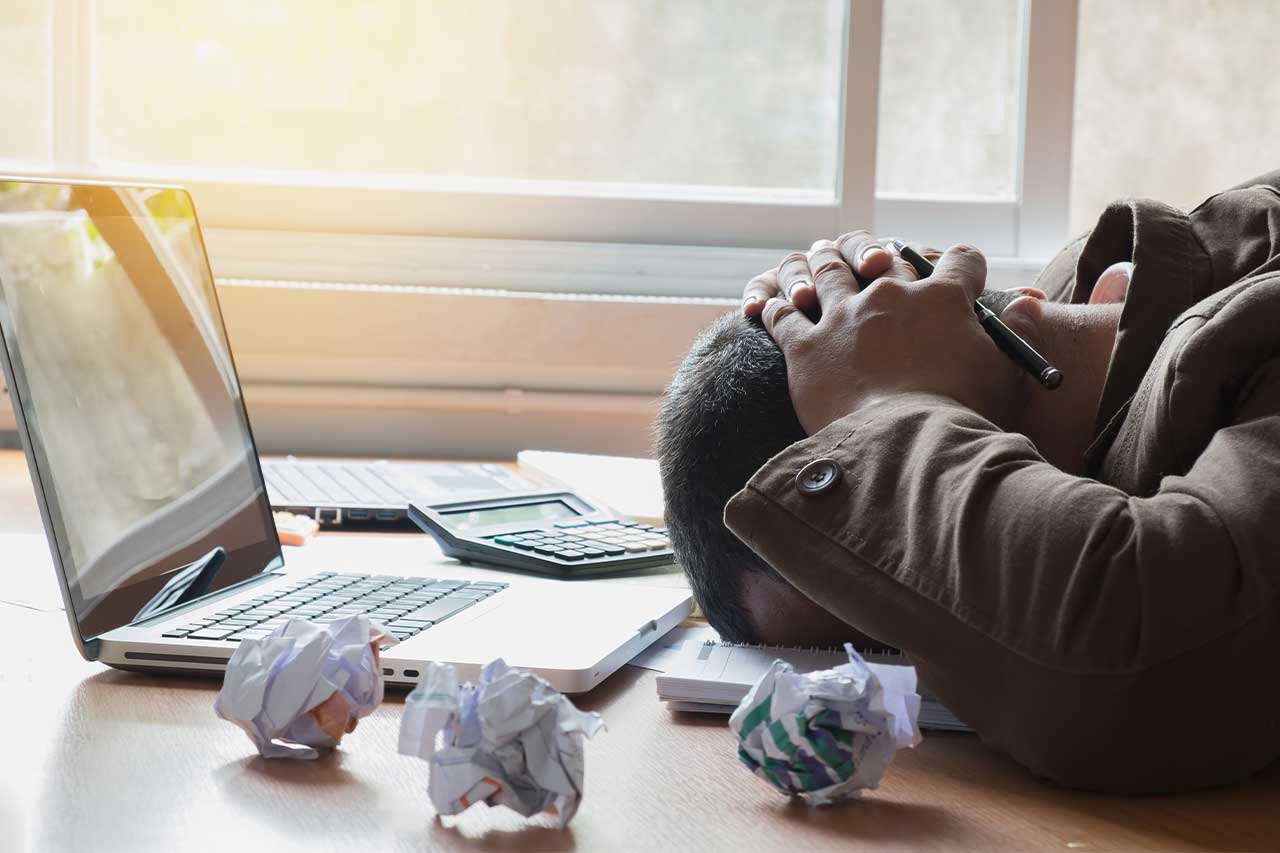 Frustrated man with head on table and paper all around him
